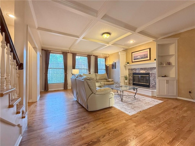 living room with coffered ceiling, built in features, beamed ceiling, a fireplace, and light wood-type flooring