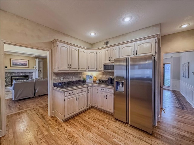 kitchen with tasteful backsplash, a high end fireplace, light hardwood / wood-style floors, and appliances with stainless steel finishes