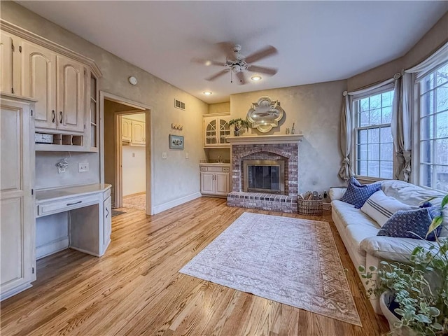 living room featuring light hardwood / wood-style floors, a brick fireplace, and ceiling fan