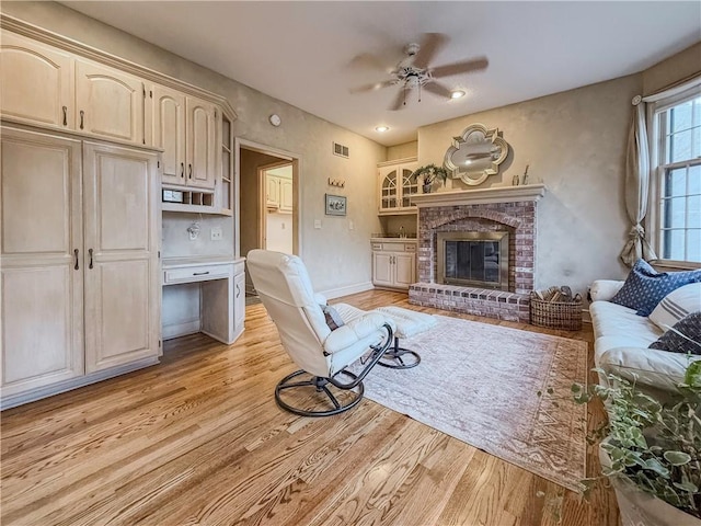 living room featuring a fireplace, light hardwood / wood-style floors, and ceiling fan