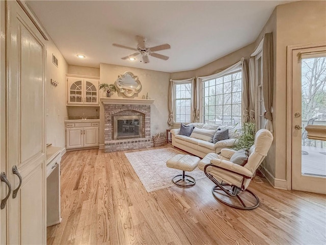 sitting room with light wood-type flooring, a brick fireplace, and ceiling fan