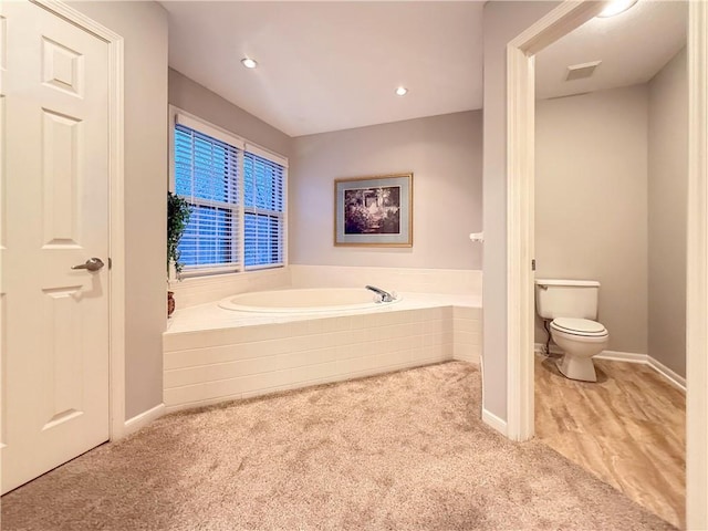 bathroom featuring a relaxing tiled tub and toilet