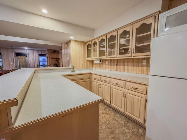 kitchen featuring wood walls, light brown cabinets, white refrigerator, sink, and kitchen peninsula