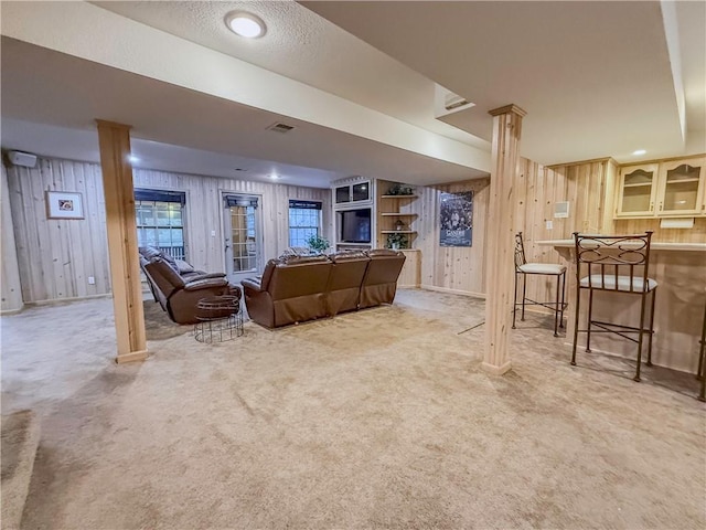 carpeted living room with bar area, wooden walls, and a textured ceiling