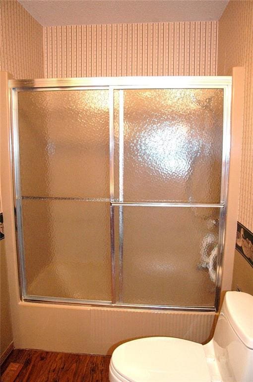 bathroom featuring wood-type flooring, toilet, and bath / shower combo with glass door