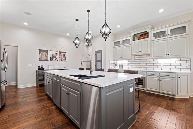 kitchen with gray cabinetry, sink, dark hardwood / wood-style flooring, decorative light fixtures, and a center island with sink