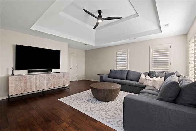 living room with a tray ceiling, ceiling fan, and dark wood-type flooring