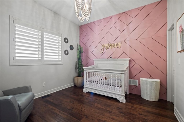 bedroom featuring a crib, dark hardwood / wood-style flooring, and a chandelier