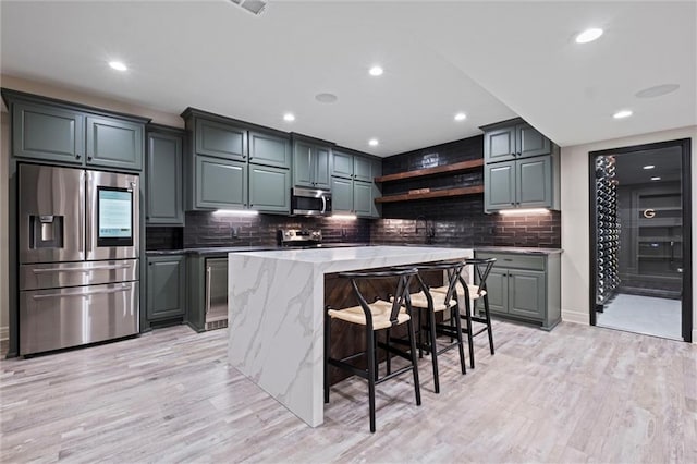 kitchen featuring appliances with stainless steel finishes, gray cabinetry, a breakfast bar, light hardwood / wood-style floors, and a kitchen island