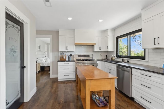 kitchen with appliances with stainless steel finishes, dark hardwood / wood-style flooring, backsplash, sink, and white cabinetry