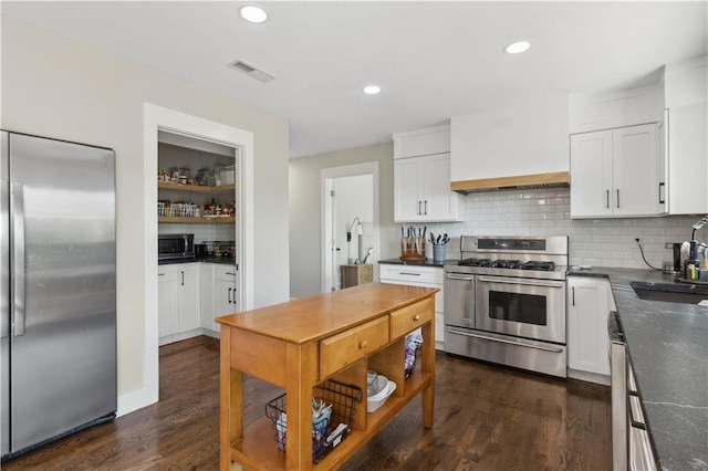 kitchen with tasteful backsplash, white cabinets, stainless steel appliances, and dark hardwood / wood-style floors