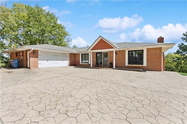 single story home featuring brick siding, a chimney, a garage, and decorative driveway