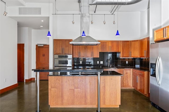 kitchen with dark stone counters, an island with sink, a high ceiling, and appliances with stainless steel finishes