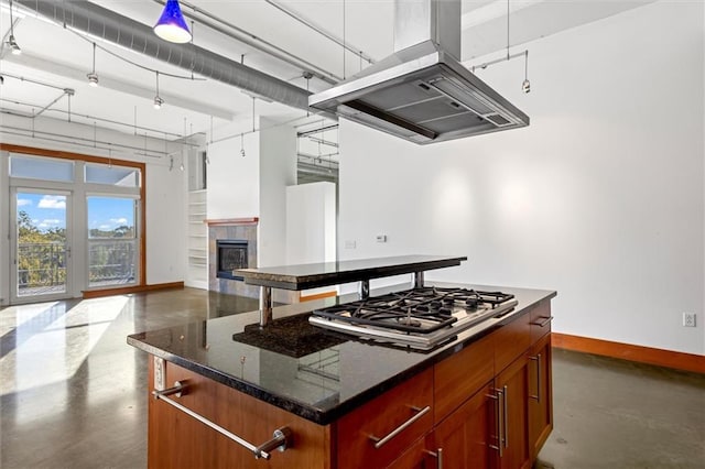 kitchen with dark stone counters, a kitchen island, island range hood, and stainless steel gas stovetop