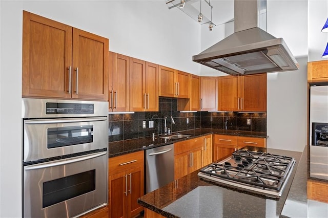 kitchen with sink, island range hood, backsplash, appliances with stainless steel finishes, and dark stone counters