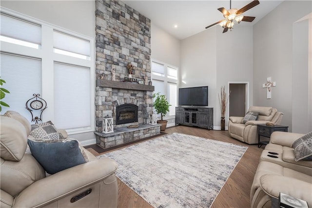 living room with a high ceiling, hardwood / wood-style floors, ceiling fan, and a fireplace