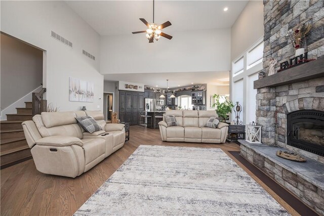 living room featuring ceiling fan with notable chandelier, a fireplace, a towering ceiling, and hardwood / wood-style flooring