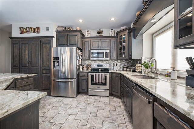 kitchen with dark brown cabinets, light stone counters, tasteful backsplash, sink, and appliances with stainless steel finishes