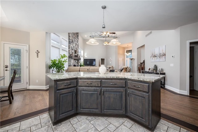 kitchen featuring light stone counters, a center island, light hardwood / wood-style flooring, dark brown cabinetry, and decorative light fixtures