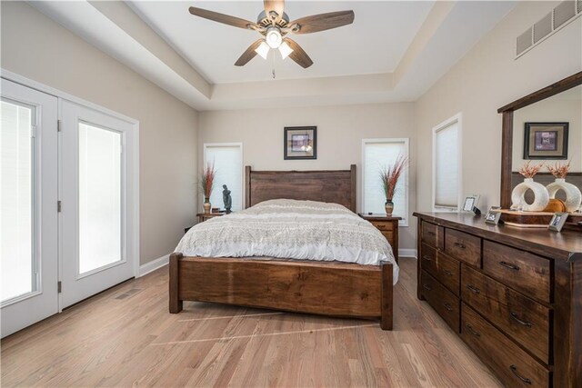 bedroom with a raised ceiling, light hardwood / wood-style floors, and ceiling fan