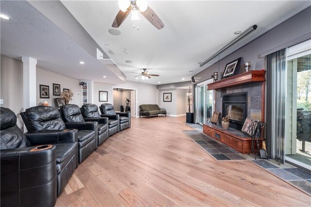 home theater room with wood-type flooring, decorative columns, ceiling fan, and a tile fireplace