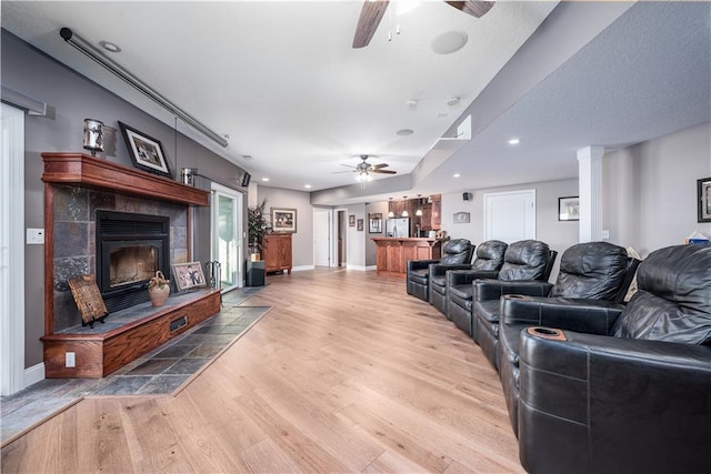 living room with a tiled fireplace, ceiling fan, hardwood / wood-style floors, and bar