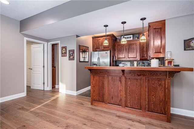 kitchen featuring pendant lighting, kitchen peninsula, a kitchen bar, hardwood / wood-style floors, and stainless steel fridge