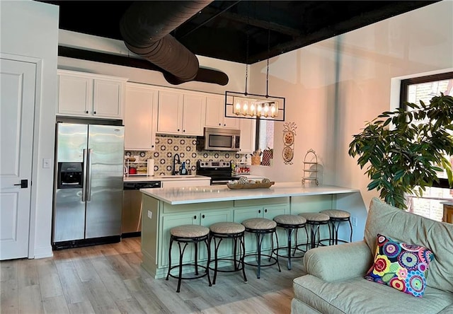 kitchen featuring a breakfast bar, pendant lighting, white cabinetry, kitchen peninsula, and stainless steel appliances