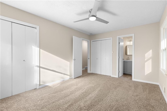 unfurnished bedroom with connected bathroom, ceiling fan, light carpet, and multiple closets