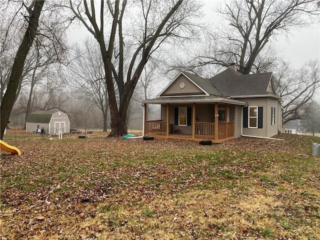 view of front of house featuring an outbuilding, a porch, a shingled roof, a shed, and a chimney