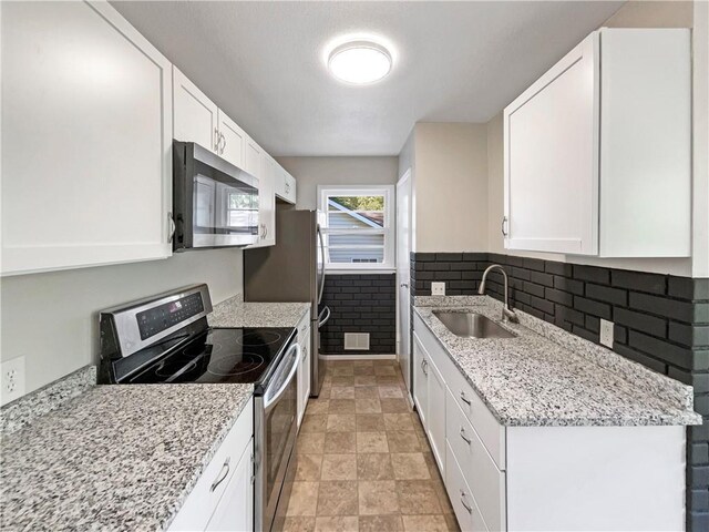 kitchen with light stone countertops, stainless steel appliances, white cabinetry, and sink