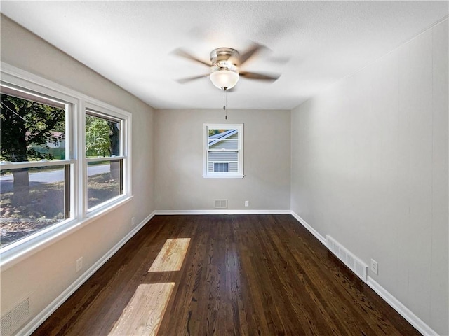 spare room featuring a healthy amount of sunlight, dark hardwood / wood-style floors, and ceiling fan