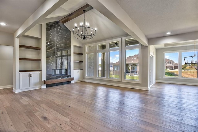 unfurnished living room featuring a tiled fireplace, hardwood / wood-style flooring, vaulted ceiling with beams, built in shelves, and a notable chandelier