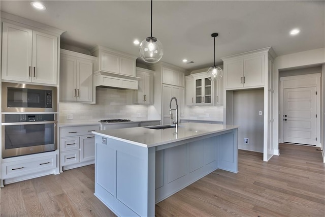 kitchen with white cabinetry, hanging light fixtures, light hardwood / wood-style flooring, stainless steel appliances, and decorative backsplash