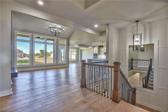 hall with vaulted ceiling, an inviting chandelier, and hardwood / wood-style floors