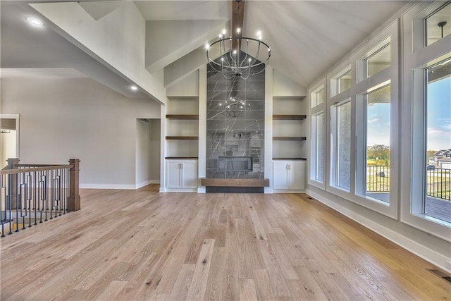 unfurnished living room featuring built in shelves, a tiled fireplace, light hardwood / wood-style flooring, and a notable chandelier