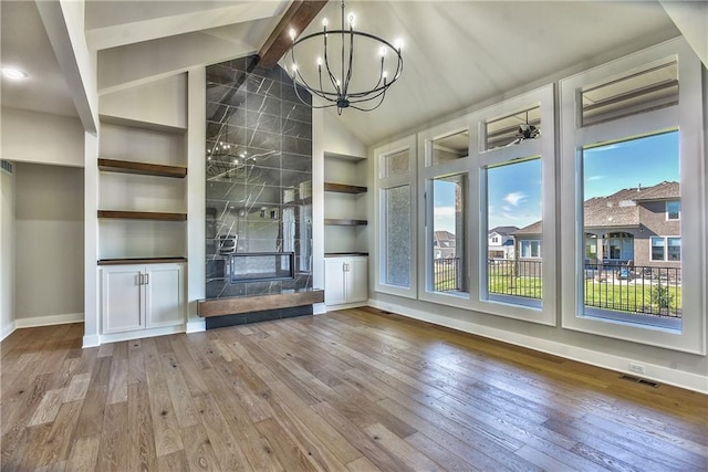 unfurnished living room featuring wood-type flooring, vaulted ceiling with beams, an inviting chandelier, and a fireplace