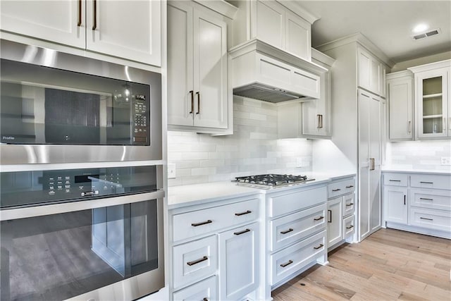 kitchen with decorative backsplash, white cabinetry, light hardwood / wood-style flooring, and stainless steel appliances