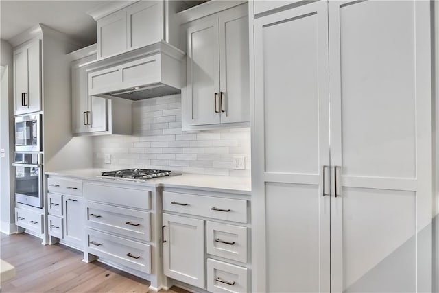 kitchen with light wood-type flooring, backsplash, white cabinetry, and custom exhaust hood