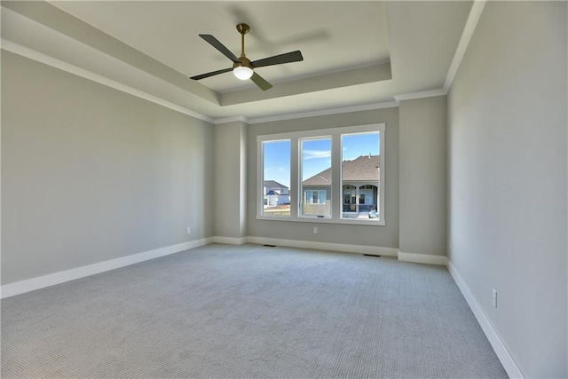 empty room with ceiling fan, light colored carpet, a tray ceiling, and crown molding