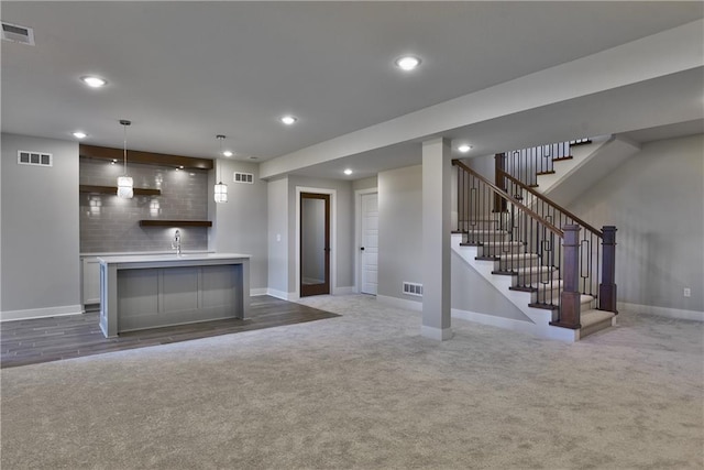 kitchen featuring hanging light fixtures, decorative backsplash, dark carpet, a kitchen island with sink, and sink