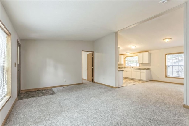 unfurnished living room with vaulted ceiling, light colored carpet, and sink