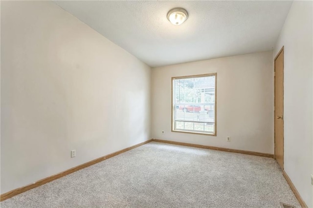 spare room with a textured ceiling, lofted ceiling, and light colored carpet