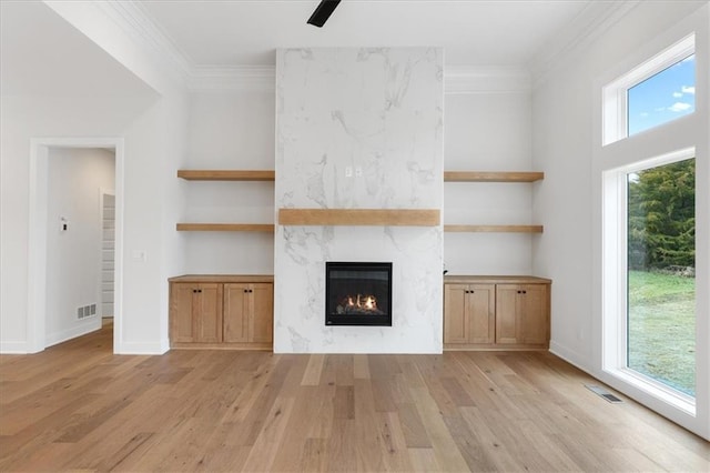 unfurnished living room featuring ornamental molding, built in features, a fireplace, light hardwood / wood-style floors, and plenty of natural light