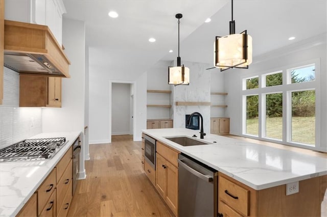 kitchen with light stone countertops, stainless steel appliances, sink, pendant lighting, and light hardwood / wood-style flooring