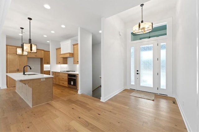 kitchen with sink, hanging light fixtures, light hardwood / wood-style flooring, oven, and a center island with sink