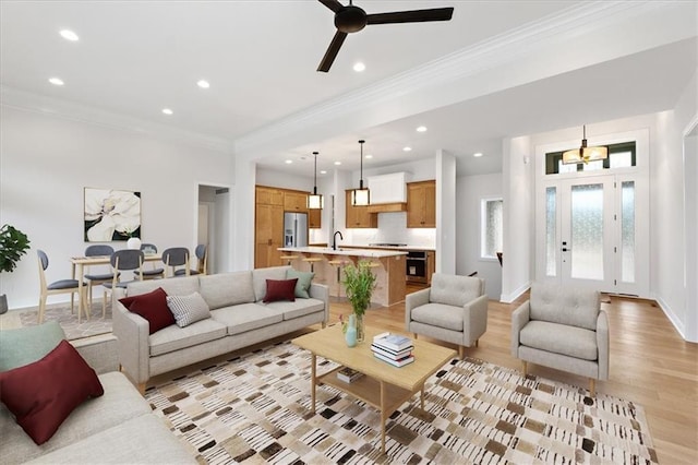 living room with light wood-type flooring, ceiling fan, ornamental molding, and sink