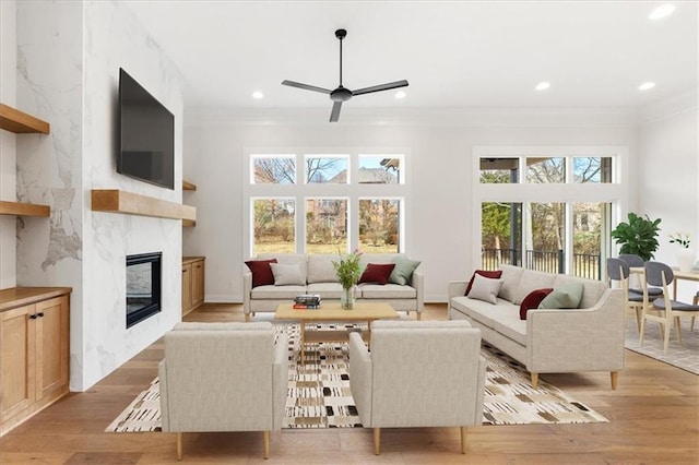 living room featuring ceiling fan, light wood-type flooring, a wealth of natural light, and a premium fireplace