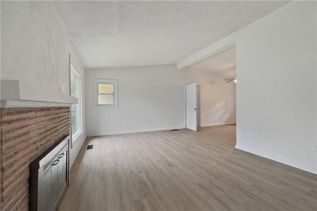 unfurnished living room featuring a textured ceiling, light hardwood / wood-style floors, lofted ceiling with beams, and a brick fireplace