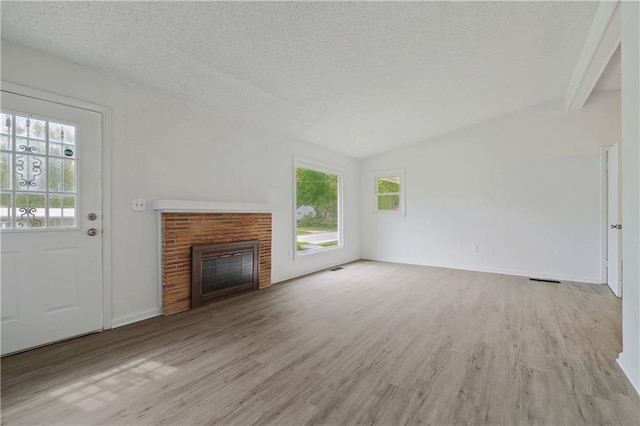 unfurnished living room featuring light wood-type flooring, a textured ceiling, vaulted ceiling, and a brick fireplace